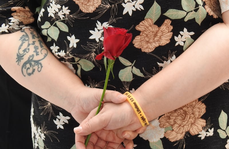 Person holding a rose behind them with a yellow lifeline awareness wristband