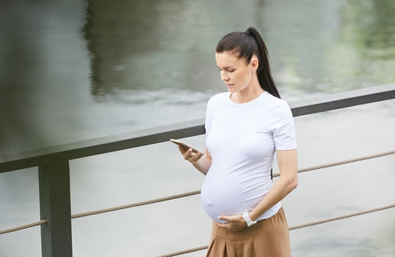 Pregnant persion walking next to a lake looking down at phone